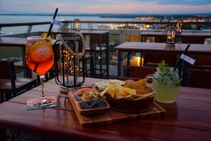 A table with a drink, a pitcher, and a bowl of snacks on a terrace overlooking a body of water.
