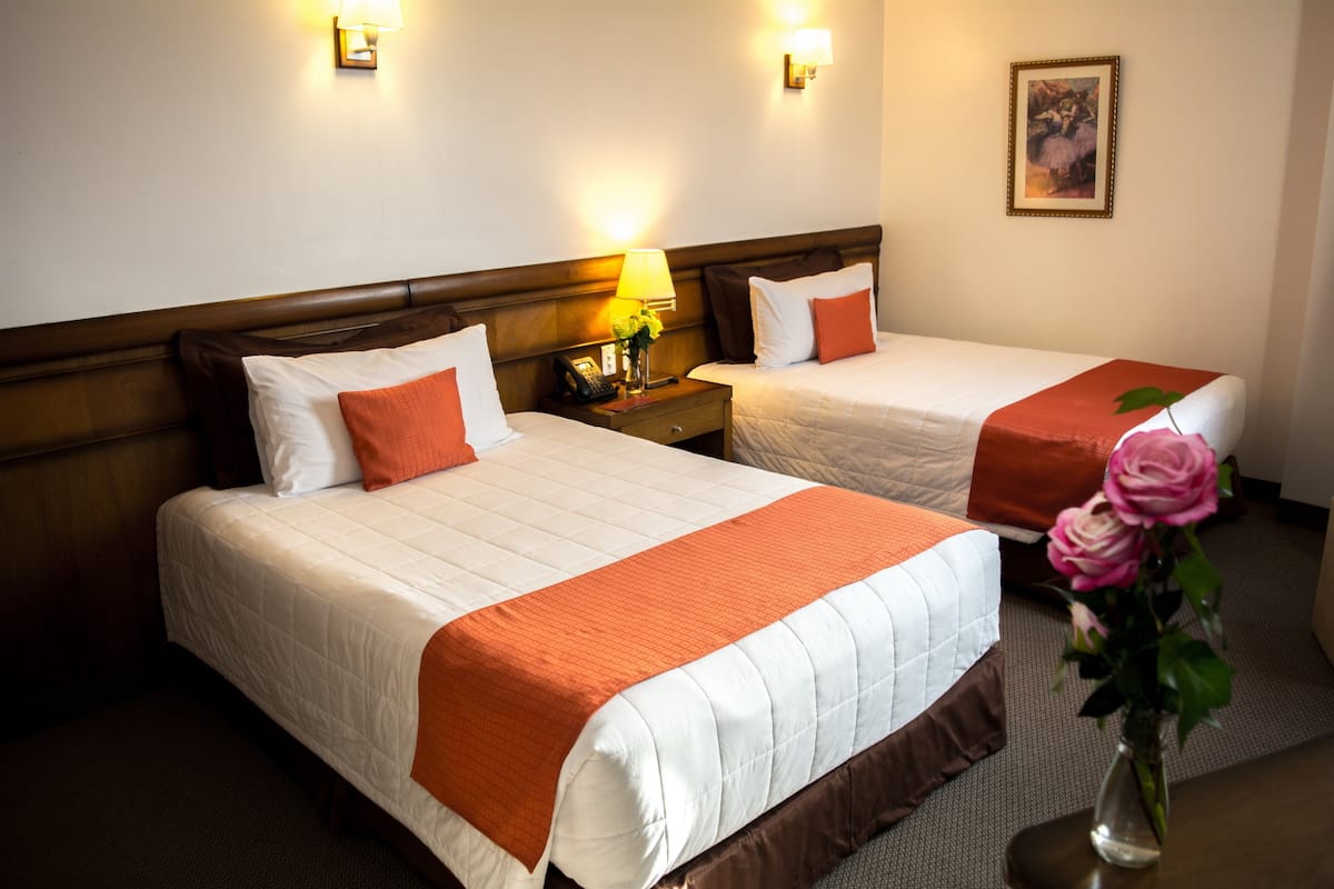 Two single beds with white and brown bedding, a nightstand with a lamp, and a vase with flowers.