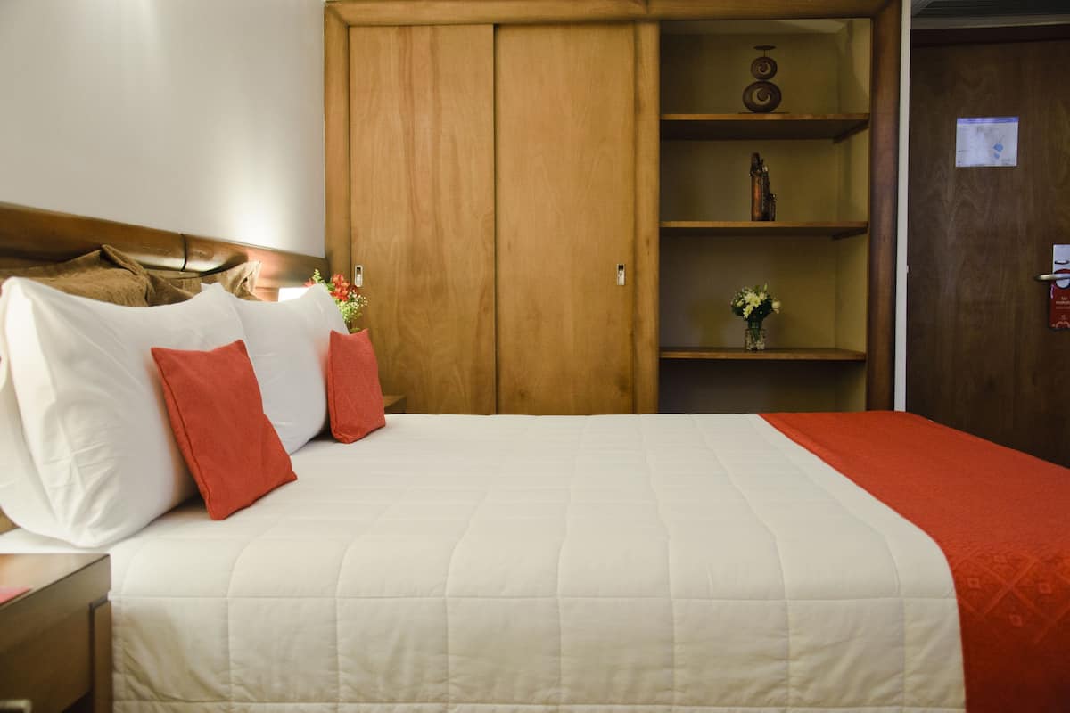 A hotel room with a bed, a wooden wardrobe, and a shelf with decorative items.