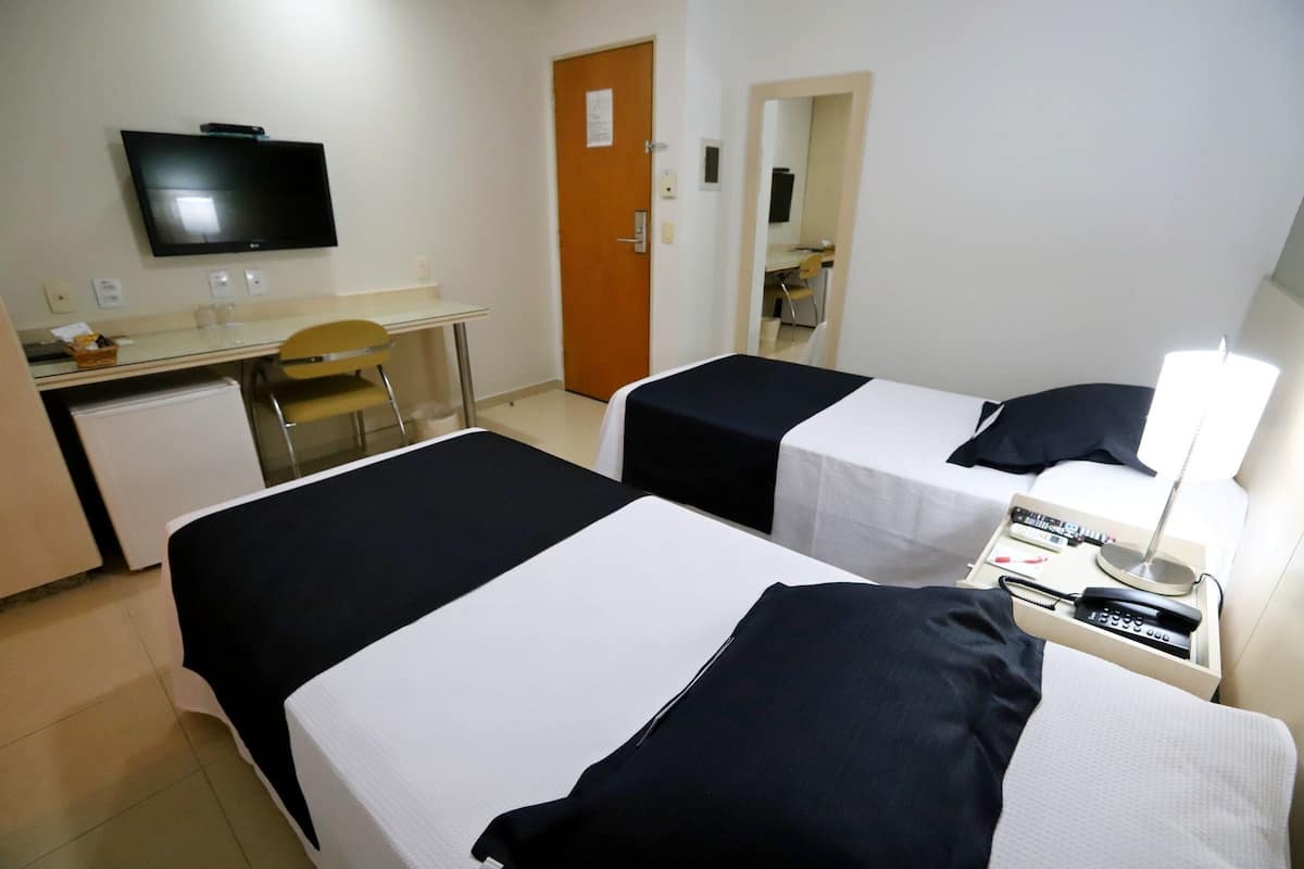 A hotel room with two beds, a desk, a chair, a television, and a door.
