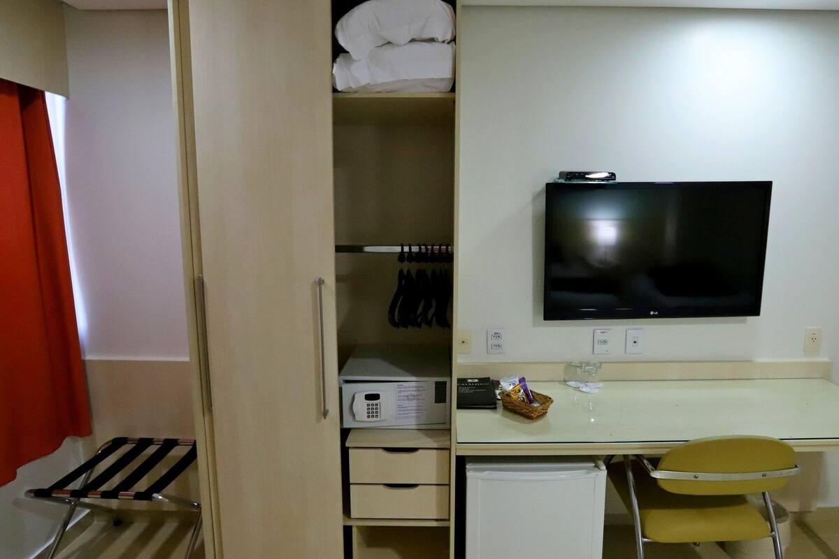 A compact hotel room with a bed, a desk with a chair, a TV, and a wardrobe.