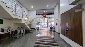 Um saguão de hotel com escada, balcão de recepção e sinalização para o elevador.