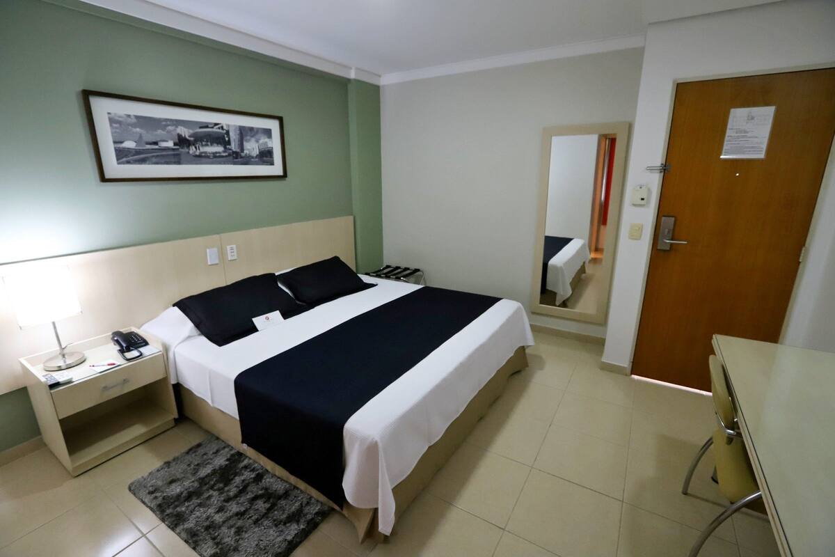 A hotel room with a bed, bedside table, lamp, and a framed picture on the wall.