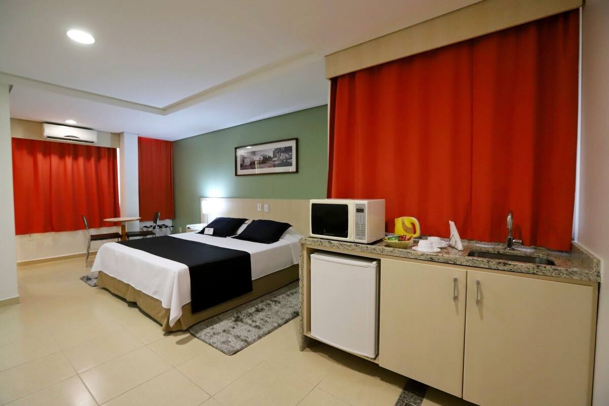 A hotel room with a bed, a desk, a microwave, a refrigerator, and a sink.