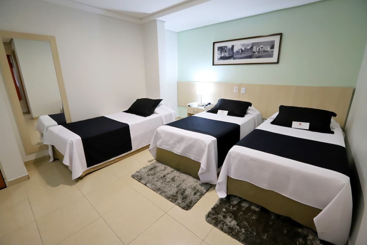 A hotel room with three single beds, each with a white and black bedspread, and a small rug on the floor.