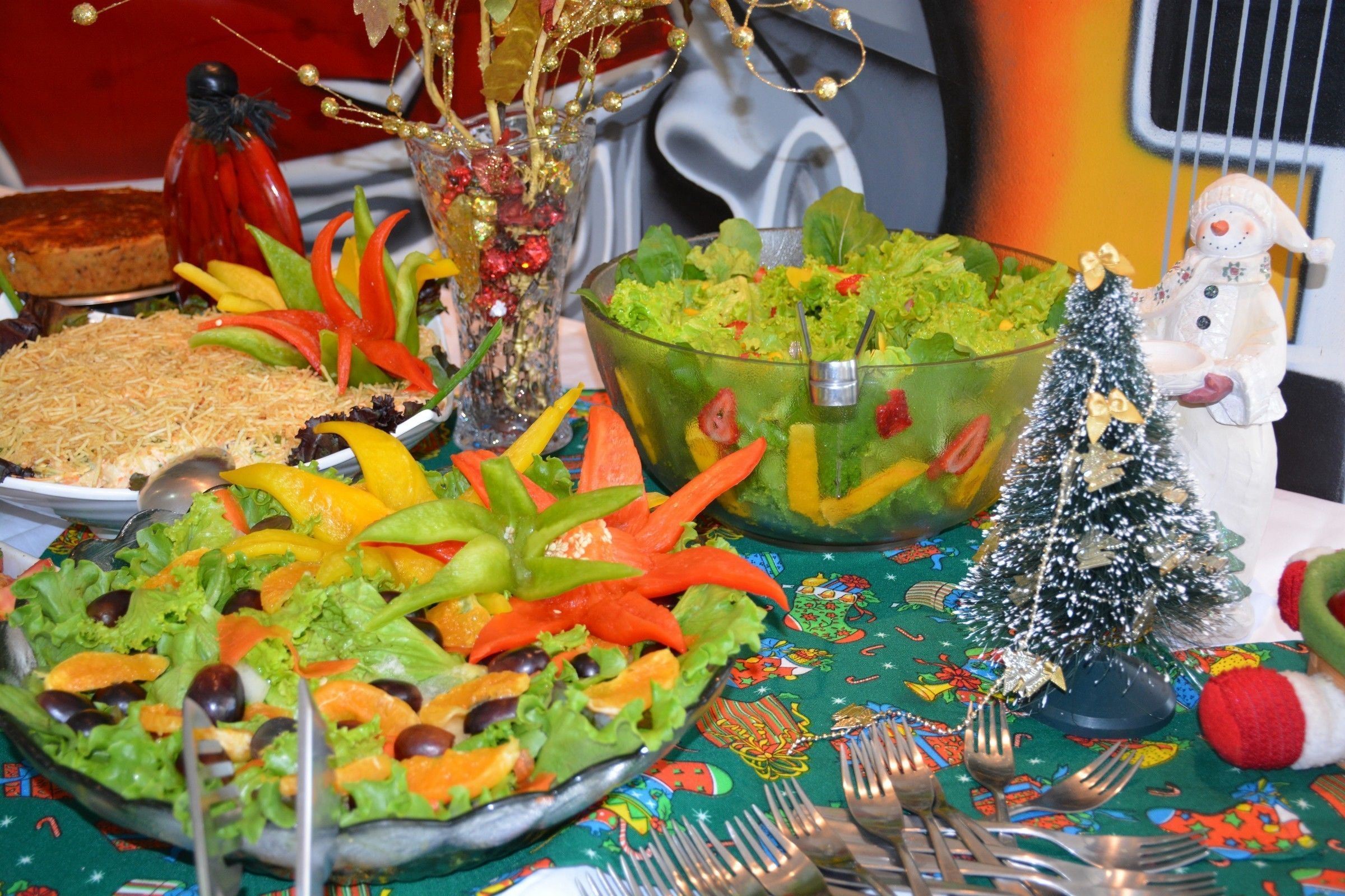 A table with various dishes, including a salad and a dish with shredded cheese, set on a tablecloth with a festive pattern.