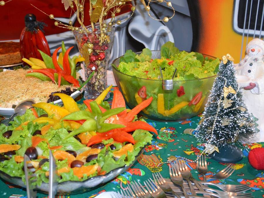 A table with various dishes, including a salad and a dish with shredded cheese, set on a tablecloth with a festive pattern.