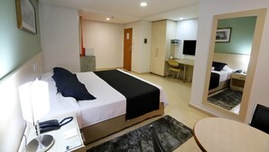 Quarto de hotel com cama, mesa de cabeceira, escrivaninha, cadeira e espelho.