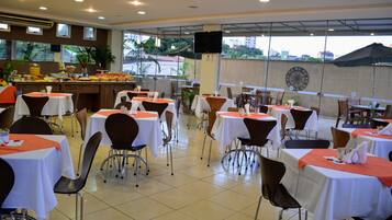 Uma sala de jantar com mesas postas para refeição, cadeiras e um buffet com diversos alimentos.