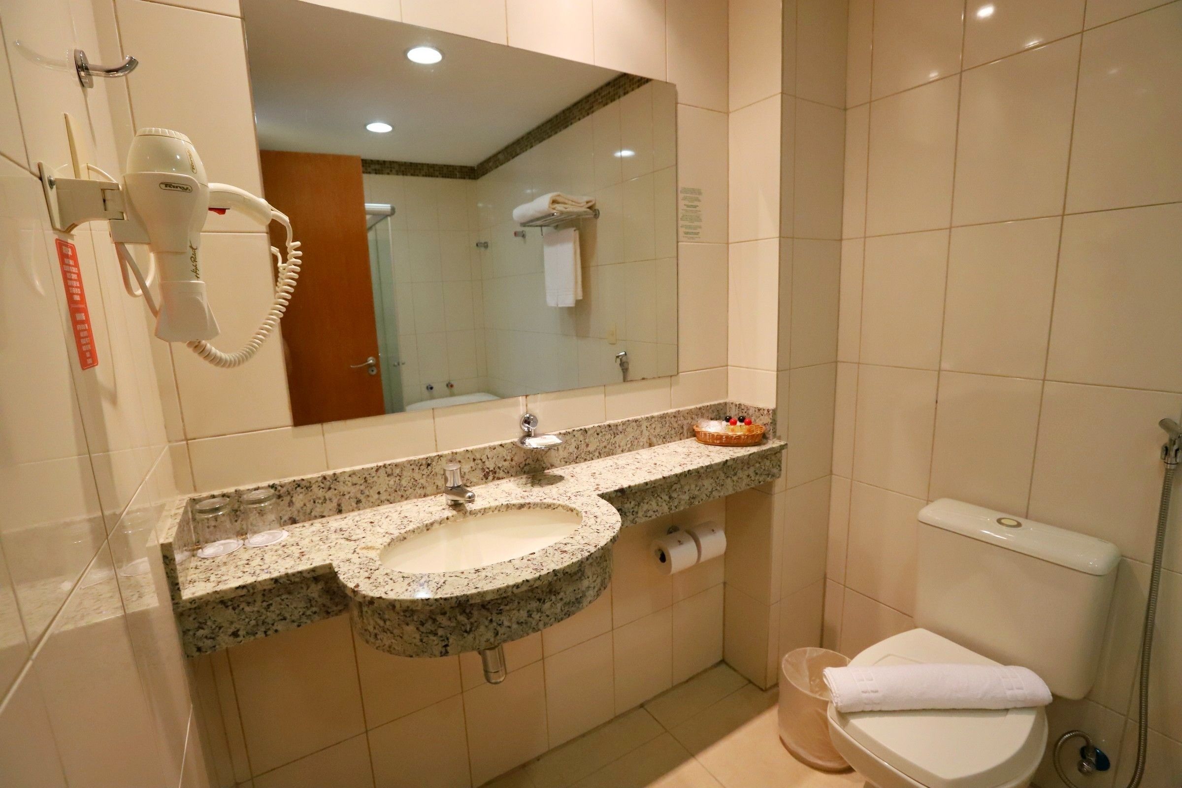 A bathroom with a granite sink, a mirror, a hairdryer, a toilet, and a shower.