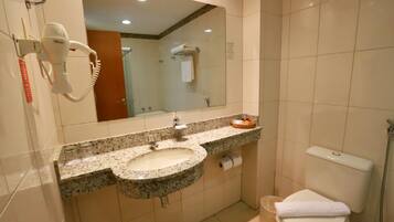 A bathroom with a granite sink, a mirror, a hairdryer, a toilet, and a shower.