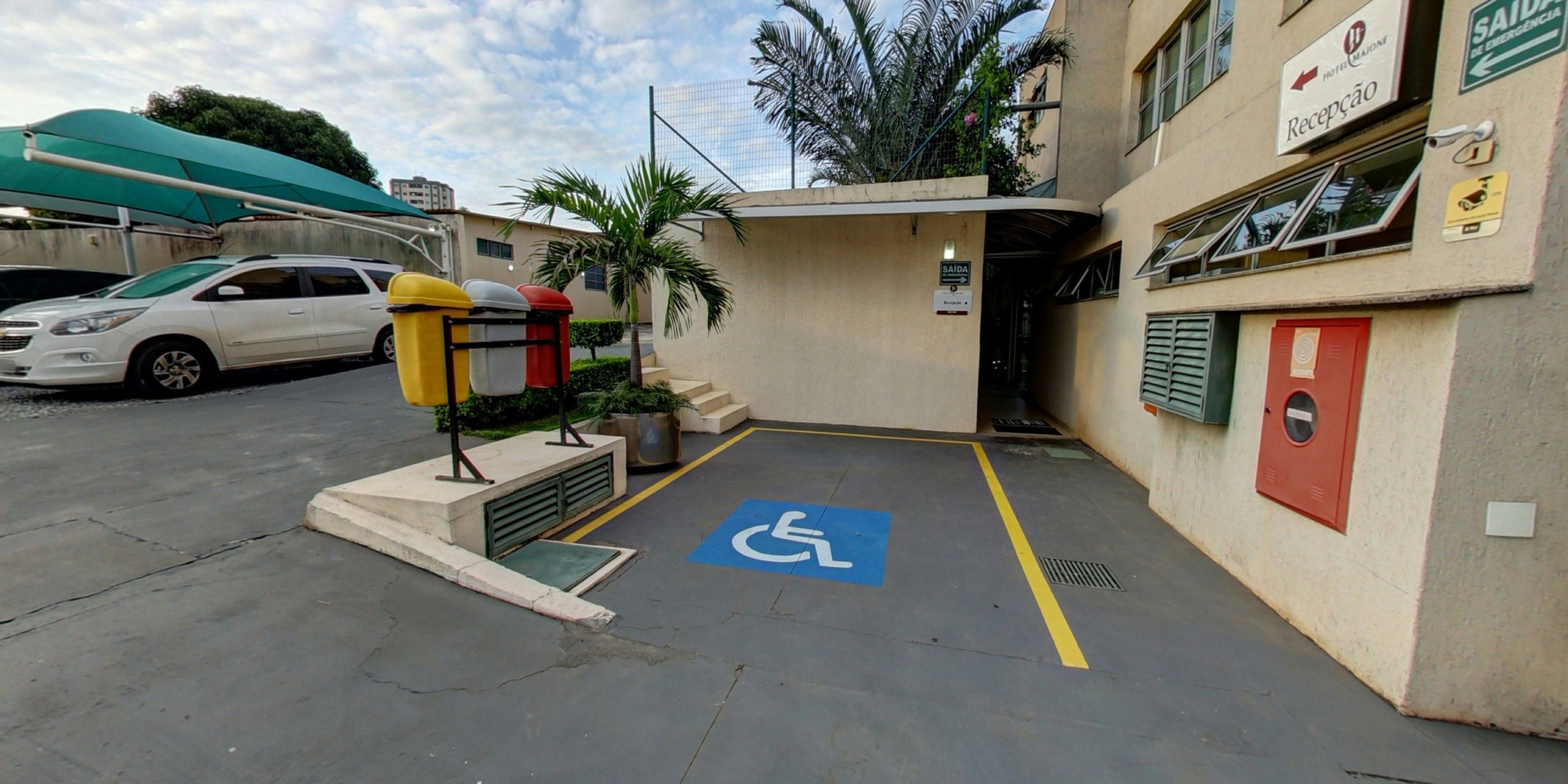 A hotel entrance with a wheelchair-accessible ramp, a parking area, and a sign indicating the reception.