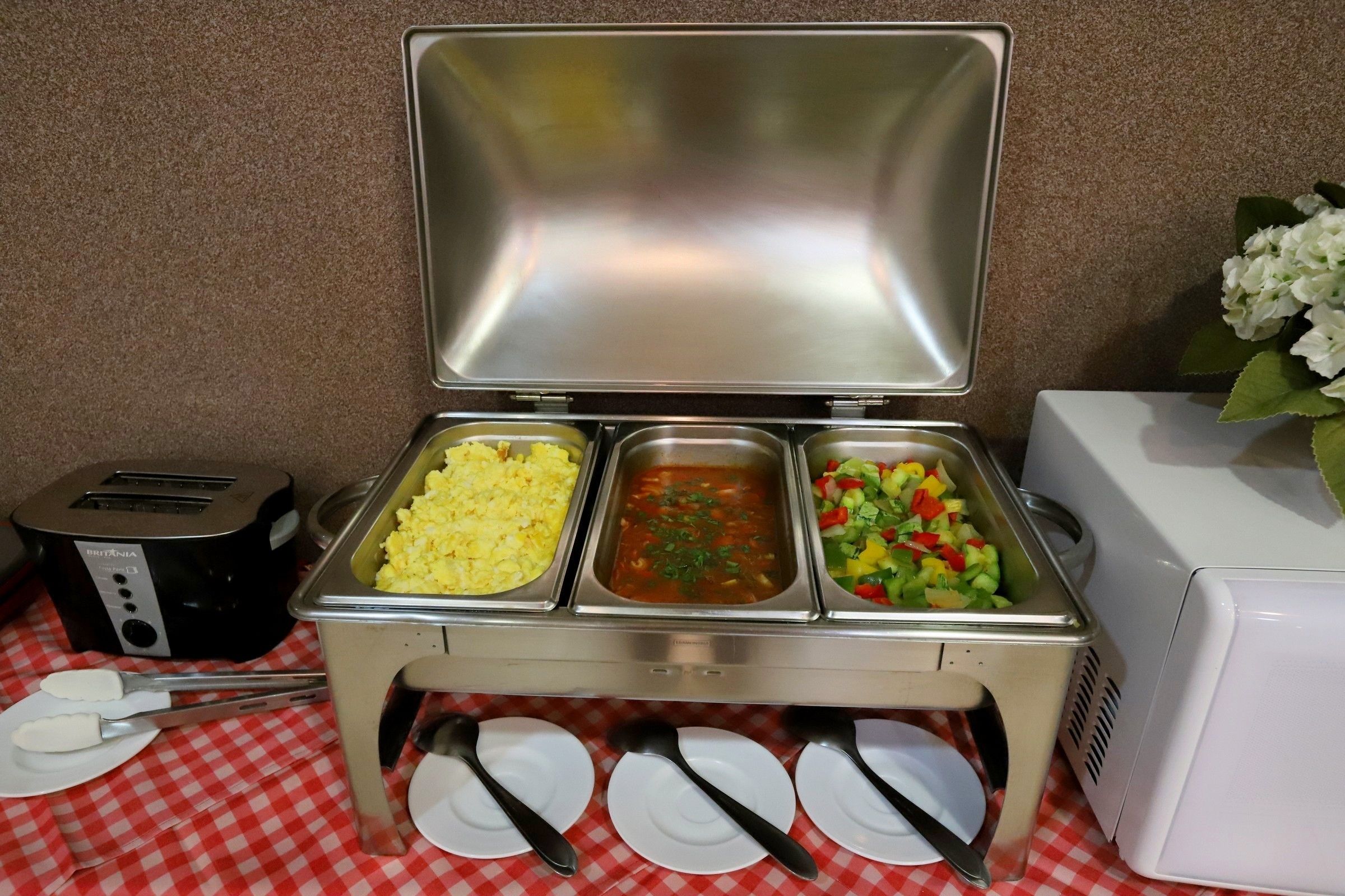 A buffet setup with scrambled eggs, tomato soup, and a vegetable salad.