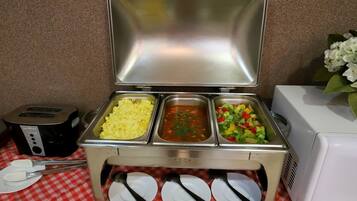 A buffet setup with scrambled eggs, tomato soup, and a vegetable salad.
