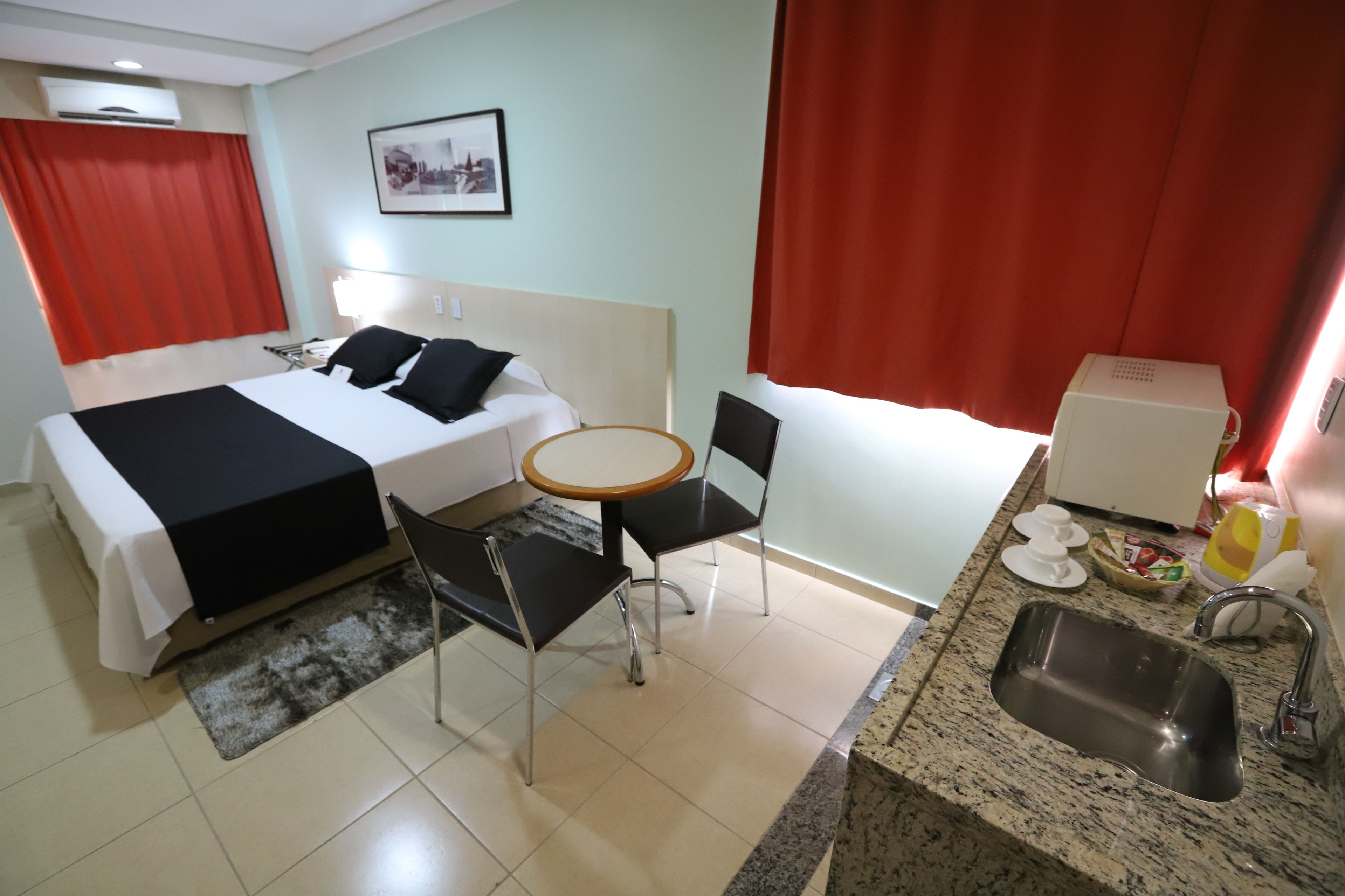 A hotel room with a bed, a small table, two chairs, a sink, and a microwave.