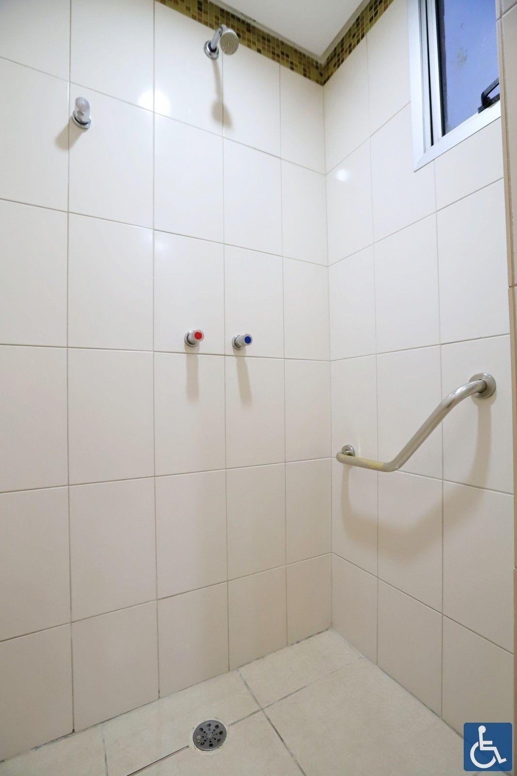 Zona de ducha con azulejos blancos, barra de apoyo y dos mandos de ducha con código de color.