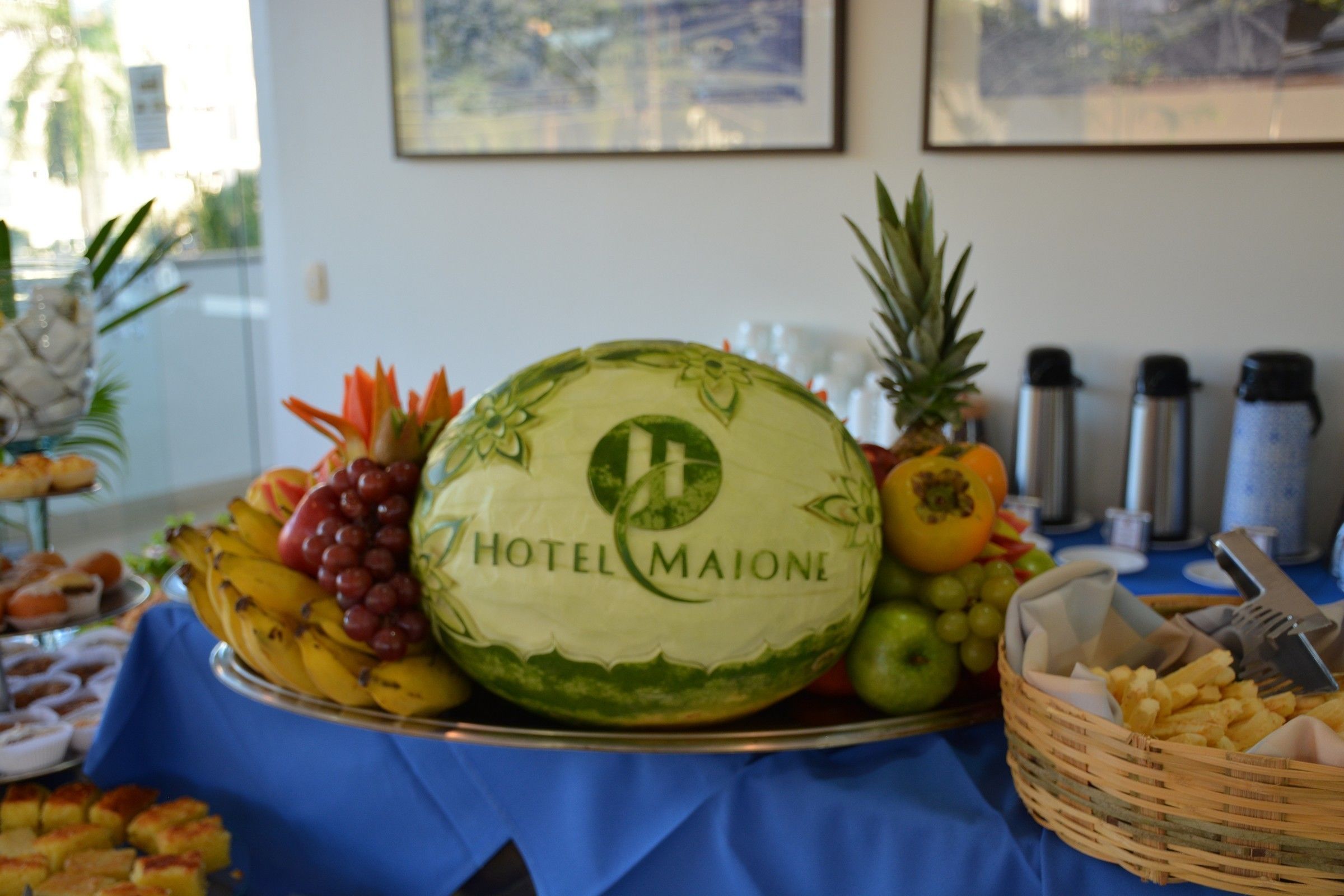 A fruit and cheese board with a watermelon labeled "Hotel Maione" at a buffet table.