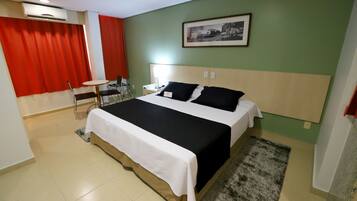 A hotel room with a bed, a desk, a chair, a small table, and a picture on the wall.