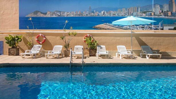 A pool area with white lounge chairs and a lifebuoy on the wall. - Jaime I (Benidorm)