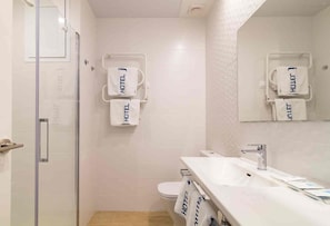 Une salle de bain moderne avec une douche à parois de verre, un lavabo blanc et deux porte-serviettes avec des serviettes portant l’inscription « HÔTEL ».