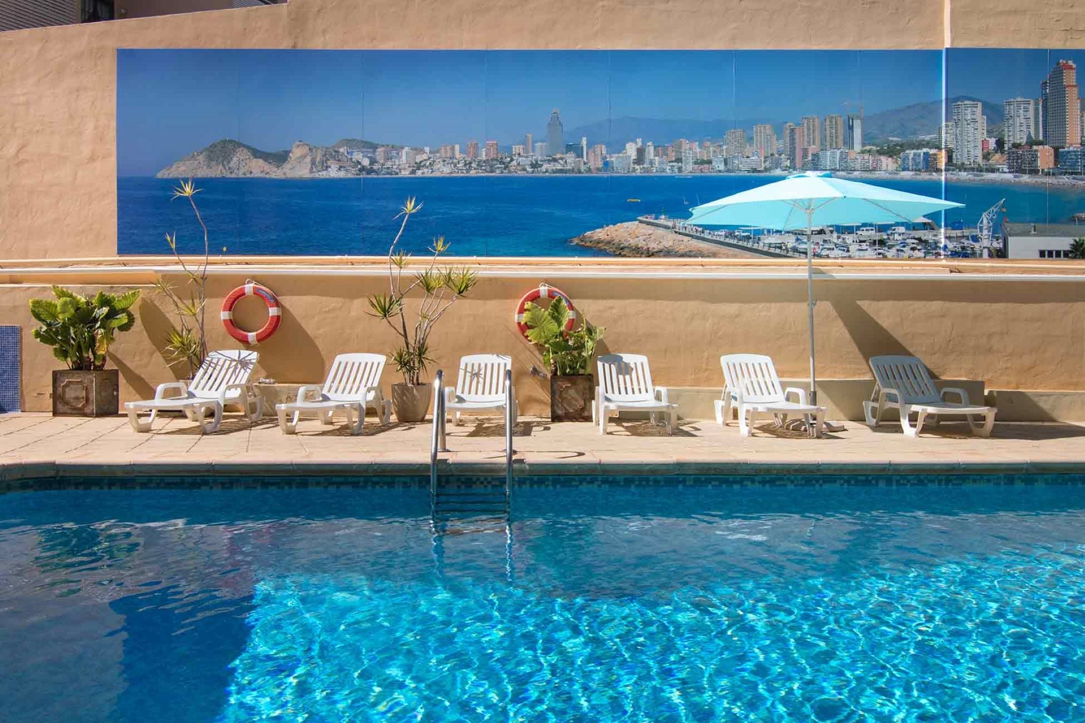 A pool area with white lounge chairs and a lifebuoy on the wall.