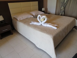 Habitación de hotel con cama, mesita de noche, lámpara y decoración de toalla con forma de cisne.