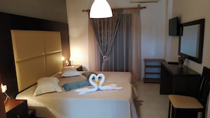 A hotel room with a bed, bedside lamps, a TV, a desk, and a chair. - Eleni's Garden & Castello Suites (Zakynthos)