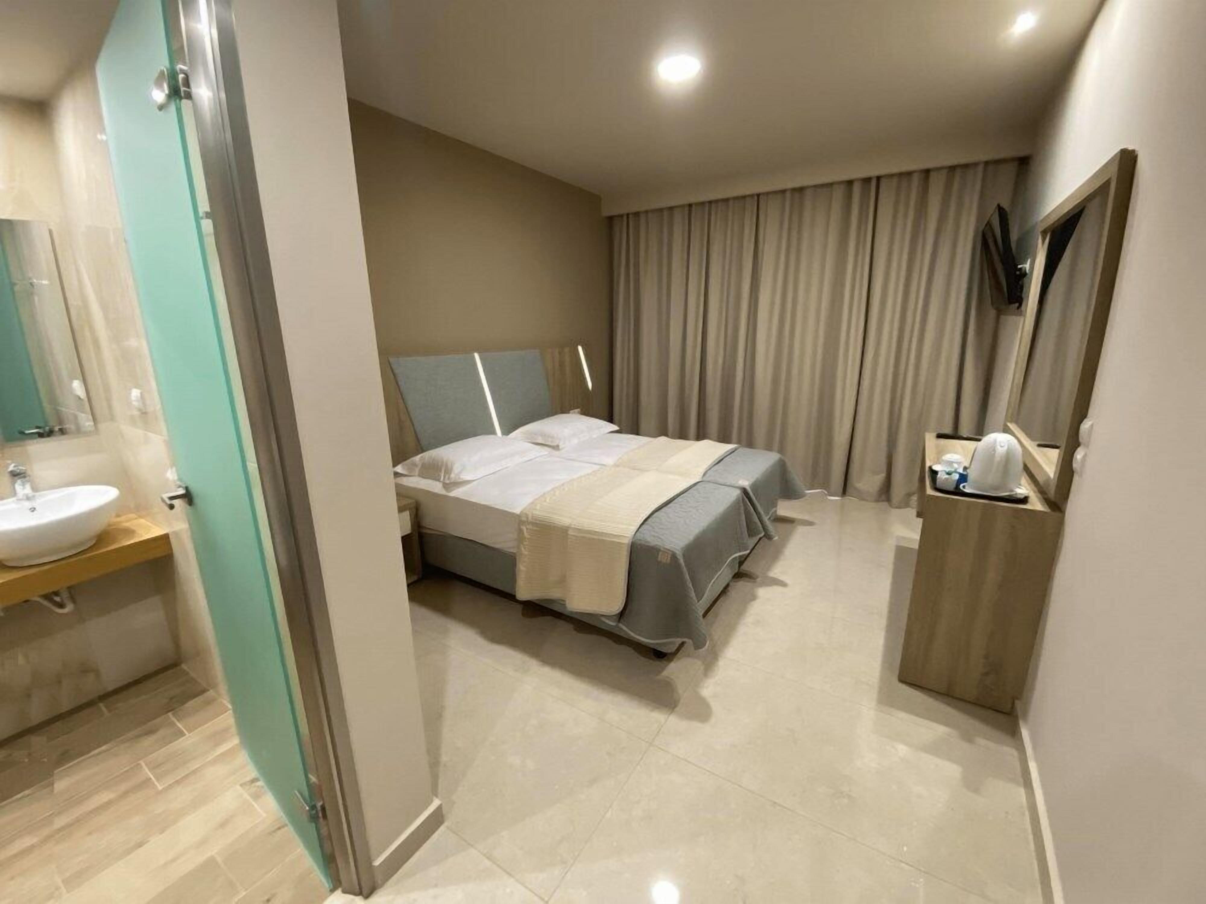 A hotel room with a bed, a bedside table, a mirror, a bathroom with a sink, and a shower area.