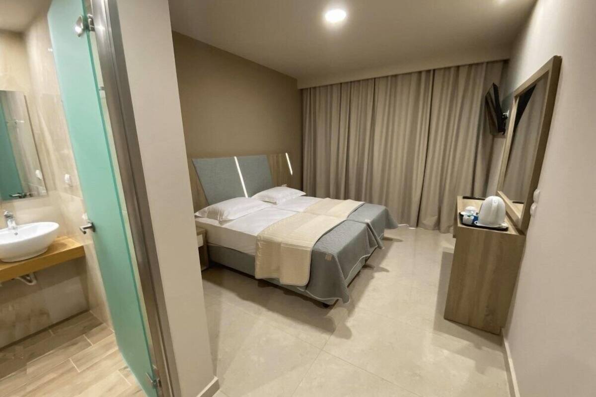 Une chambre d’hôtel comprenant un lit, une table de chevet, un miroir, une salle de bain avec un lavabo et un espace douche.