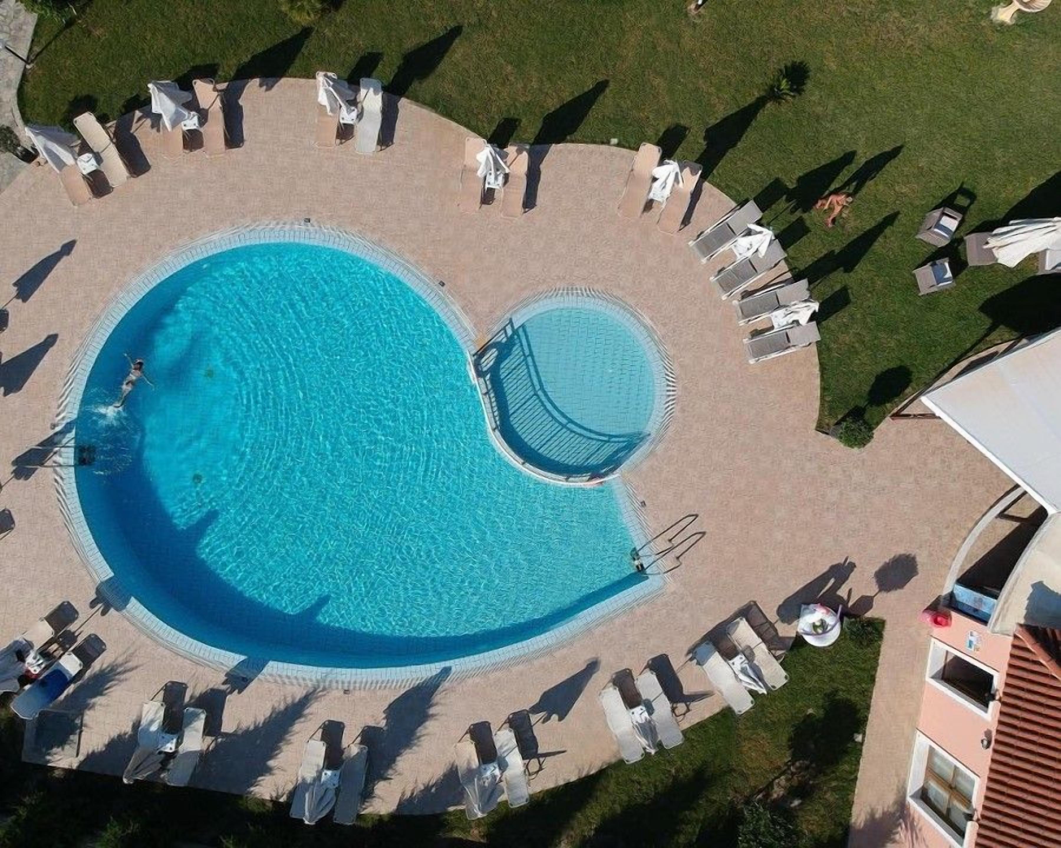 Vista aerea di una piscina con un solarium circolare, circondata da lettini e ombrelloni.