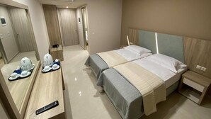A hotel room with two beds, a desk with a tray of breakfast items, a remote control, and an air conditioning unit. - Eleni's Garden & Castello Suites (Zakynthos)