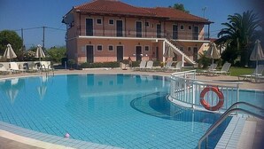 A swimming pool with a lifebuoy, lounge chairs, and a building with a balcony in the background. - Eleni's Garden & Castello Suites (Zakynthos)