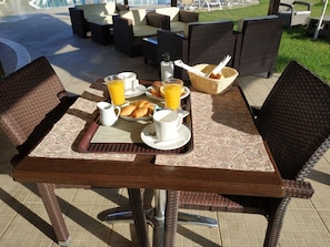 A breakfast table set with croissants, orange juice, and coffee, surrounded by wicker chairs and a view of outdoor seating. - Eleni's Garden & Castello Suites (Zakynthos)