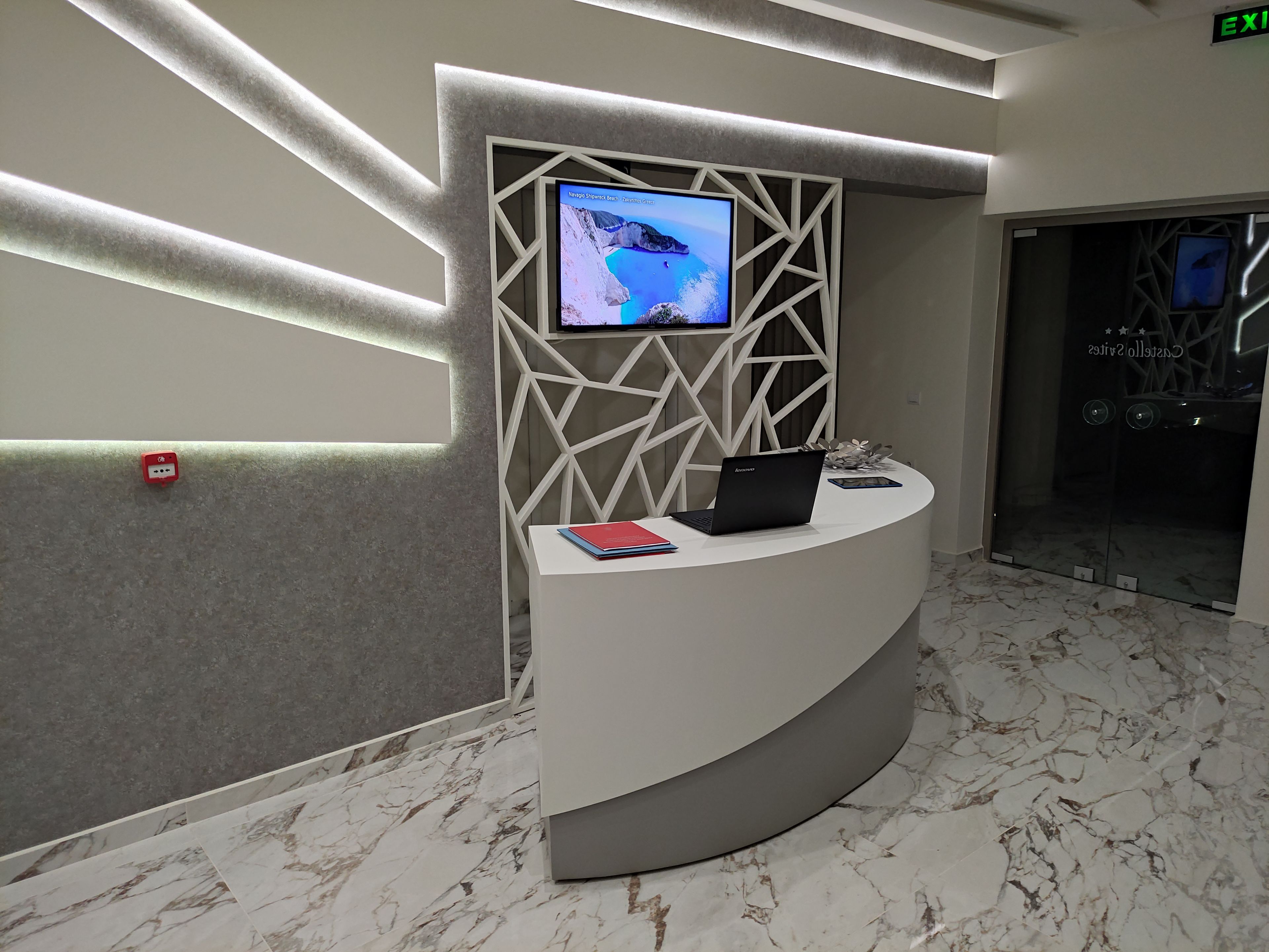 A reception desk with a monitor, a laptop, and a red book.