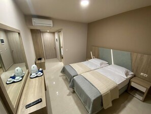 A hotel room with two beds, a desk with a tray of breakfast items, a remote control, and an air conditioning unit. - Eleni's Garden & Castello Suites (Zakynthos)