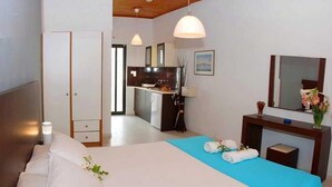 A bedroom with a bed, bedside table, and a view of the kitchen. - Eleni's Garden & Castello Suites (Zakynthos)