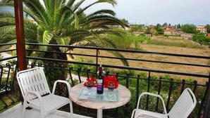 A balcony with two white chairs and a table, a bottle of wine, and two wine glasses. - Eleni's Garden & Castello Suites (Zakynthos)