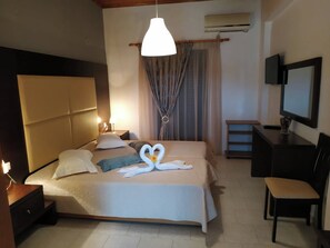 A hotel room with a bed, bedside lamps, a TV, a desk, and a chair. - Eleni's Garden & Castello Suites (Zakynthos)