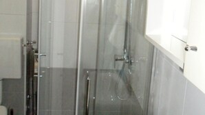 A glass-enclosed shower stall with a handheld showerhead and a wall-mounted faucet.