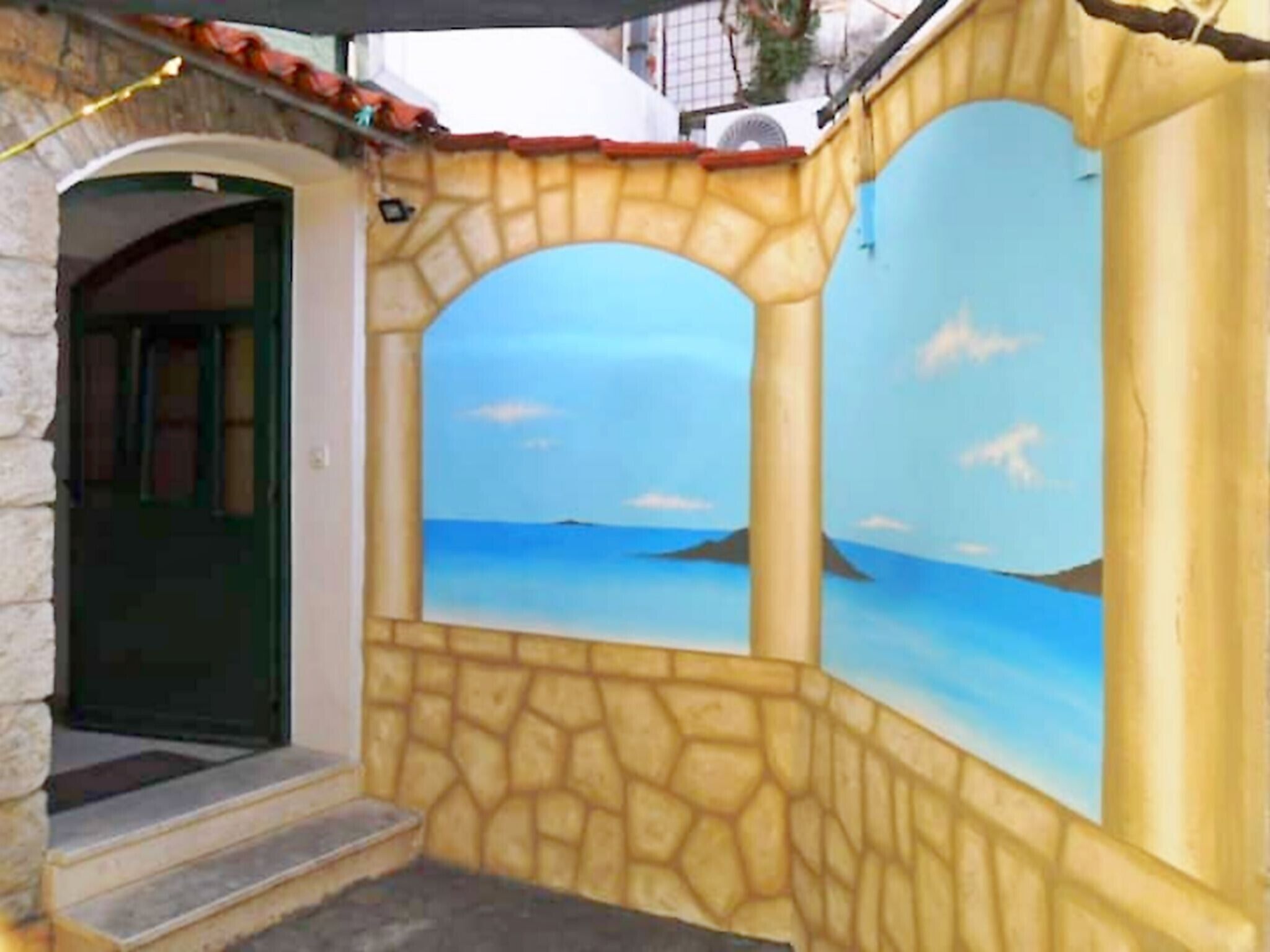 A stone facade with a mural of a sea view, a door, and a small set of steps leading to the entrance.