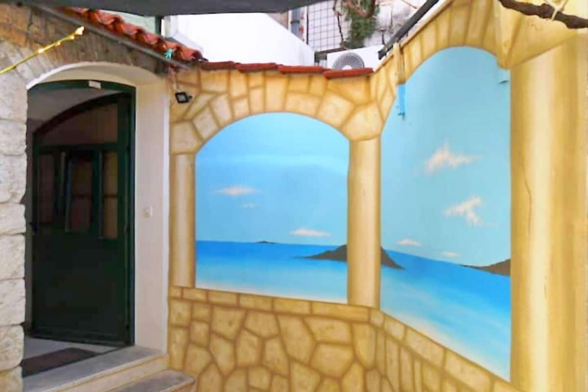 A stone facade with a mural of a sea view, a door, and a small set of steps leading to the entrance.