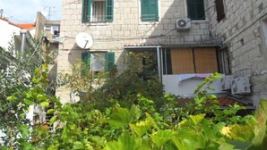 A stone building with green shutters, a satellite dish, and a small garden area.