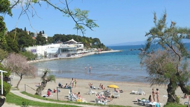 A beach with a building, trees, and clear blue water.