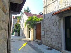A narrow street with stone buildings, a visible door, and a yellow arrow pointing to the street. - Villa Dube (Split)