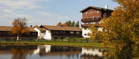 A lakeside hotel with a reflection in the water, featuring a prominent building with a balcony and a smaller attached structure.