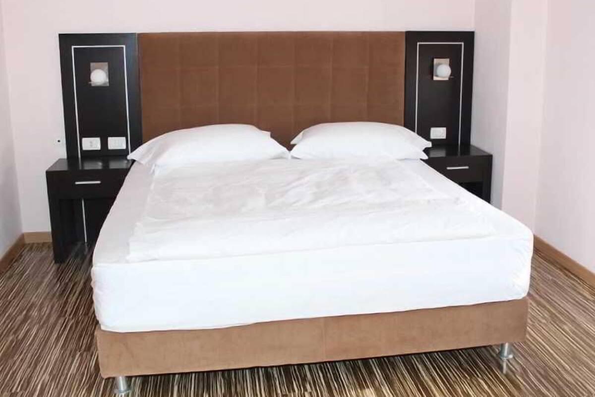A neatly made bed with a brown headboard, two bedside tables with lamps, and a striped carpet.