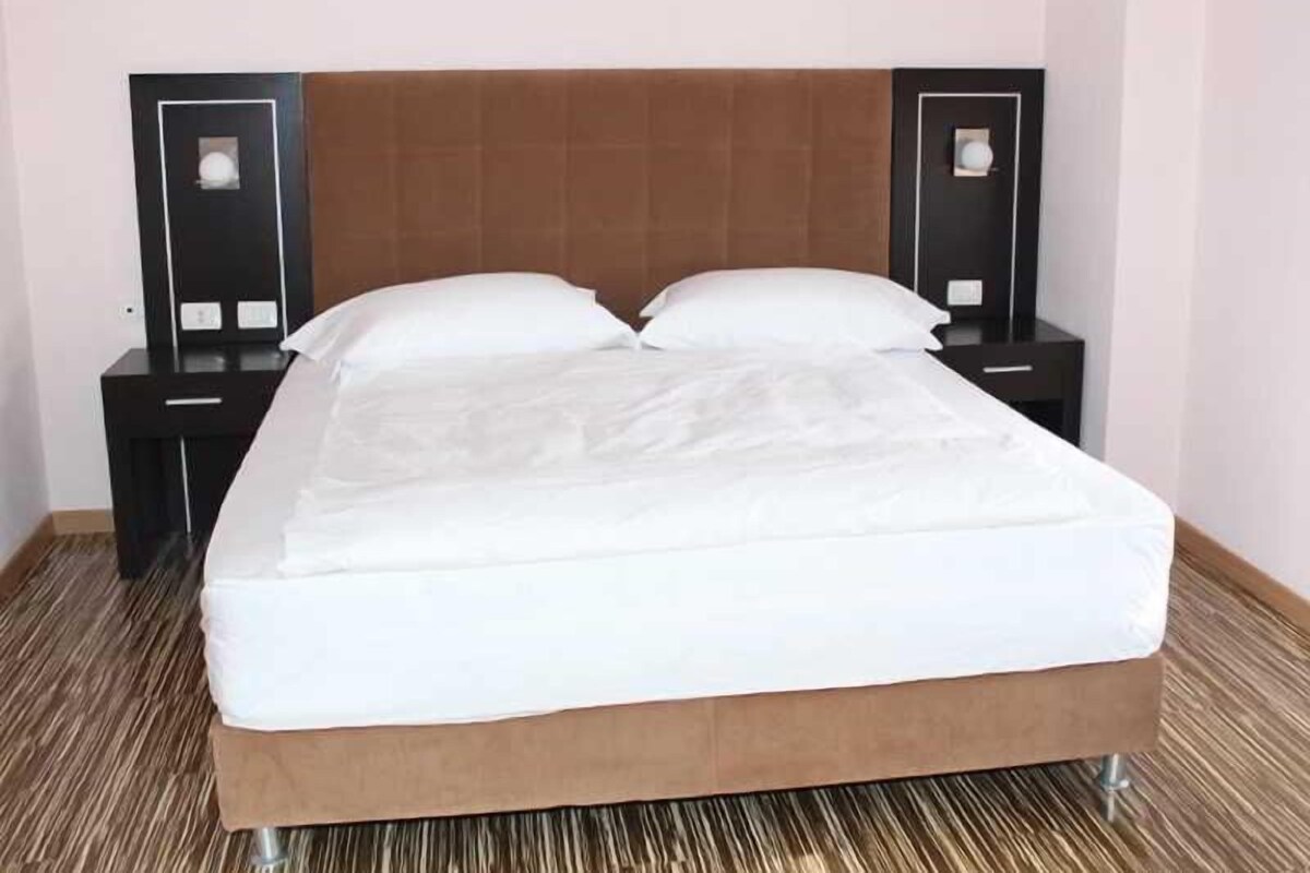 Una habitación de hotel con una cama, dos mesitas de noche y un cabecero.