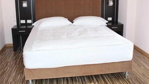 Quarto de hotel com cama, duas mesas de cabeceira e encosto de cama.