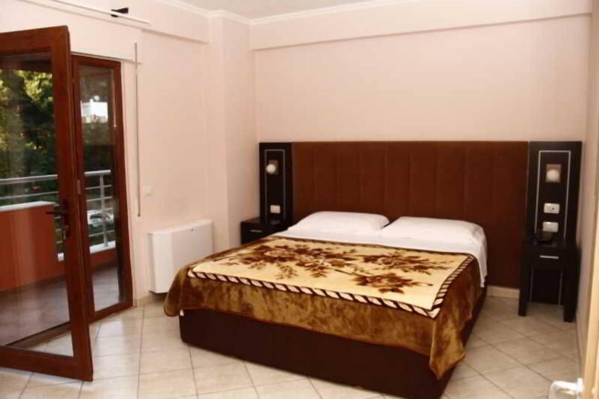 A bedroom with a bed, a wooden headboard, a nightstand, a bedside table, and a sliding glass door leading to a balcony.