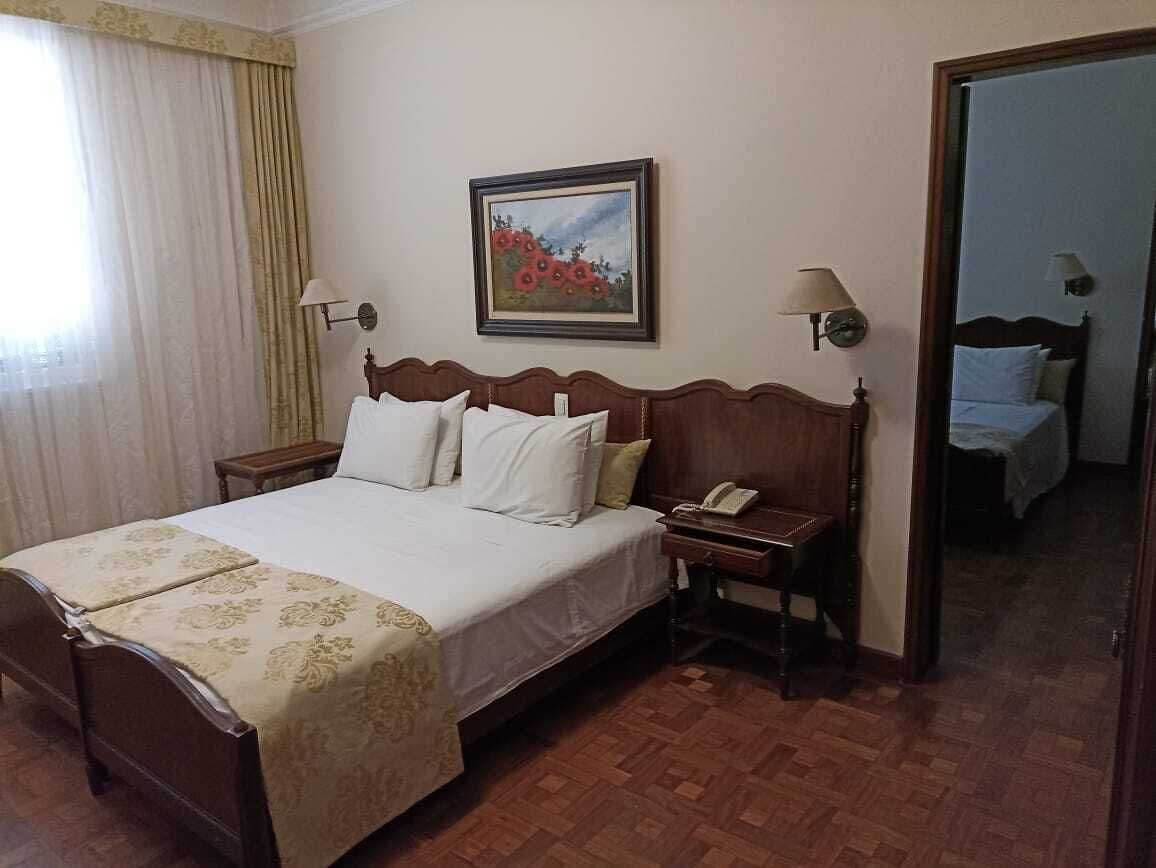 Une chambre d’hôtel avec un grand lit, deux tables de chevet, une commode, un tableau au mur et un miroir.